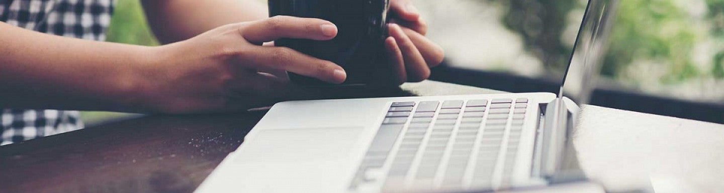 Person holding a coffee mug next to an open laptop